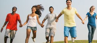 Eine Gruppe junger Menschen rennt über eine Wiese, sich an den Händen haltend und lächelnd