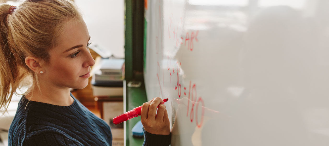 Studentin schreibt mit rotem Stift eine Formel auf ein Whiteboard.