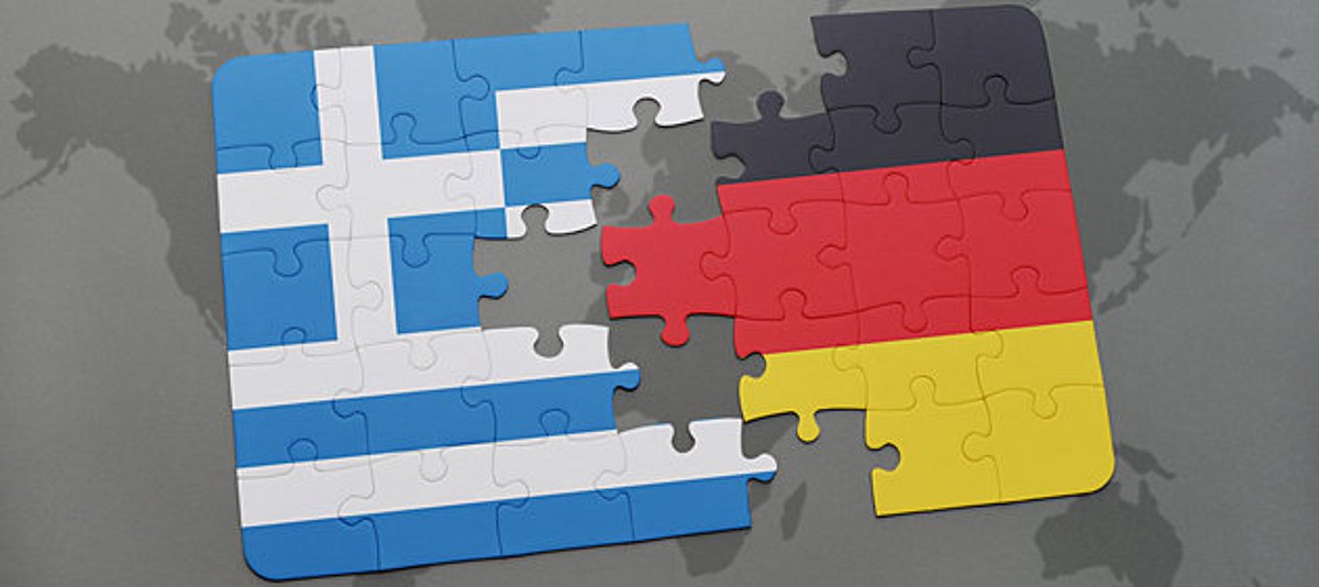 Teile der deutschen und griechischen Flagge als Puzzle vor einem Schatten der Weltkarte