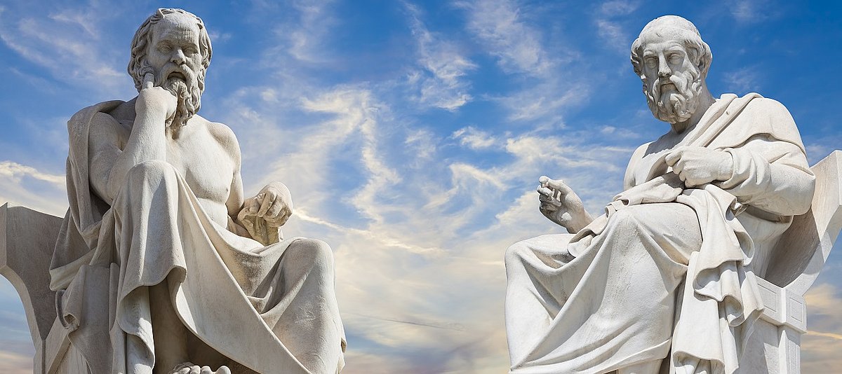 Zwei Skulpturen der sitzenden Philosophen Platon und Sokrates vor blauem Himmel