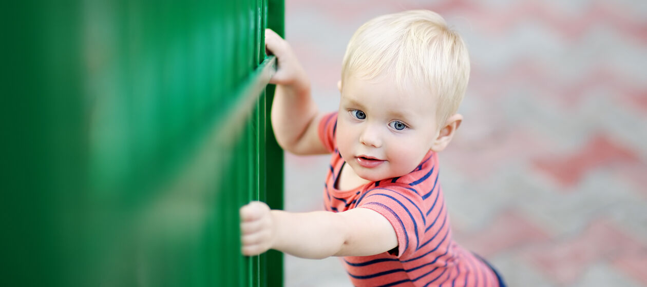 Kleinkind hält sich an einem Zaun fest
