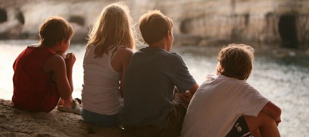 Drei Jungen und ein Mädchen sitzen auf einer Klippe am Meer im Sonnenuntergang.
