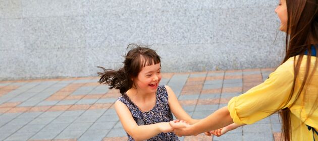 Ein Mädchen mit Down-Syndrom schleudert sich händehaltenden und freudig mit einem älteren Mädchen im Kreis