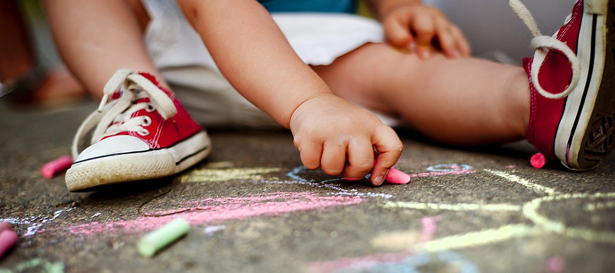 Kind sitzt auf Boden und malt mit Kreide