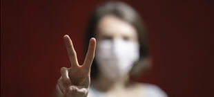 Frau mit Mundschutz zeigt ein Victory Zeichen mit ihrer Hand