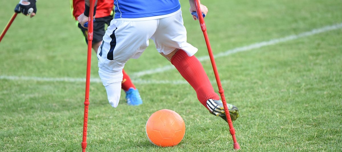 Ein Fußballer mit einem amputierten Bein spielt auf dem Rasen, im Hintergrund ist ein gegnerischer Spieler zu sehen