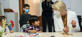 Bundesministerin Karliczek mit FFP2-Maske spricht mit einem Jungen über gemeinsam Gebasteltes.
