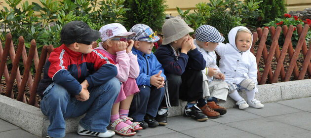 Eine Gruppe Kinder sitzt in einer Reihe an einem Jägerzaun und schaut nach links.