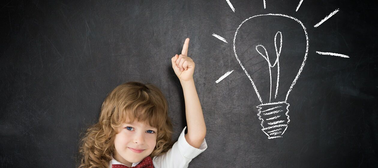 Ein Kind steht vor einer Tafel, auf die eine Glühbirne gezeichnet ist
