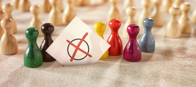 Einfarbige Spielfiguren stehen im Hintergrund und ein paar bunte Spielfiguren stehen mit einem Wahlzettel im Vordergrund. 