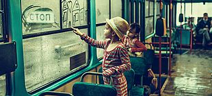 Ein Kind malt an eine beschlagene Busscheibe ein Haus