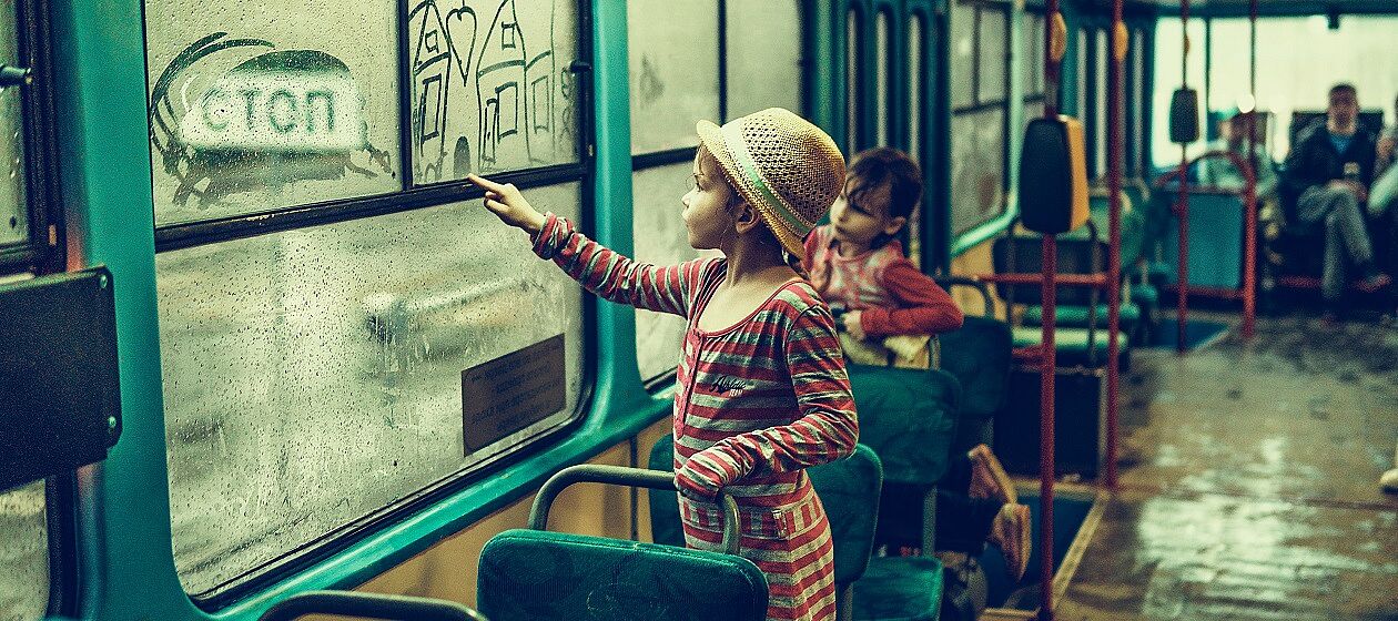 Ein Kind malt an eine beschlagene Busscheibe ein Haus