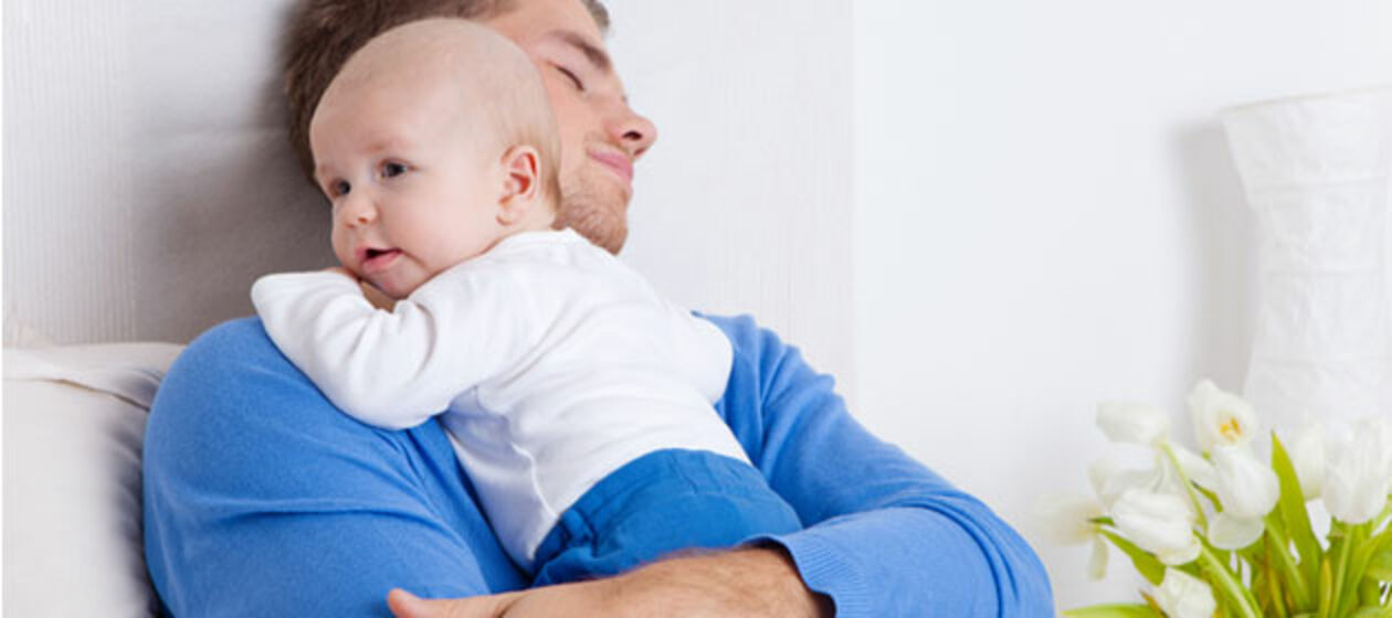 Ein Vater mit geschlossenen Augen und Baby auf dem Arm