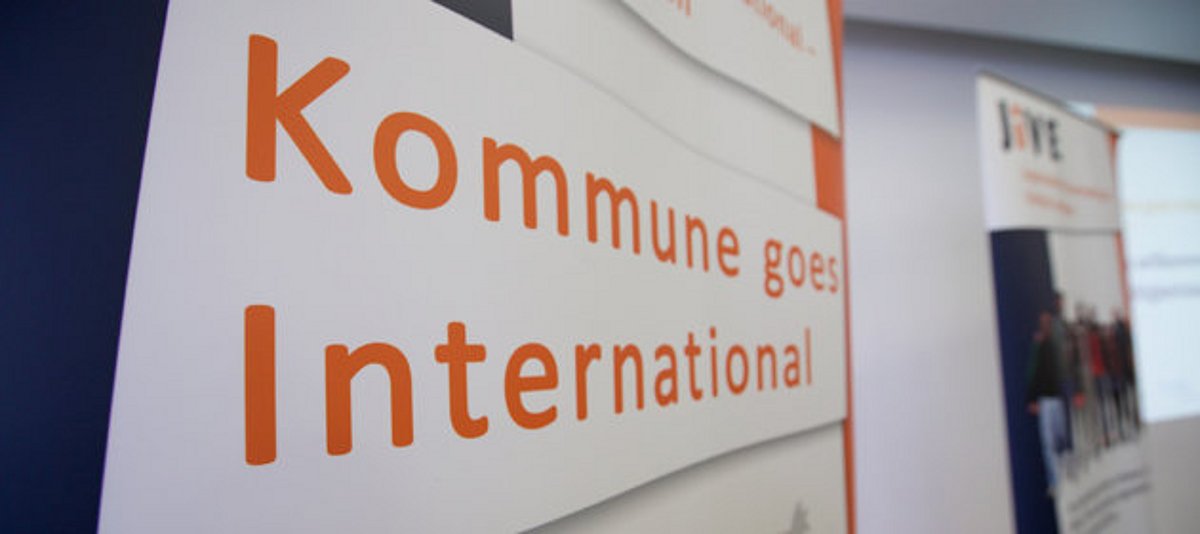 Fotoausschnitt mit Schriftzug "Kommune goes International" auf einem Roll-Up 