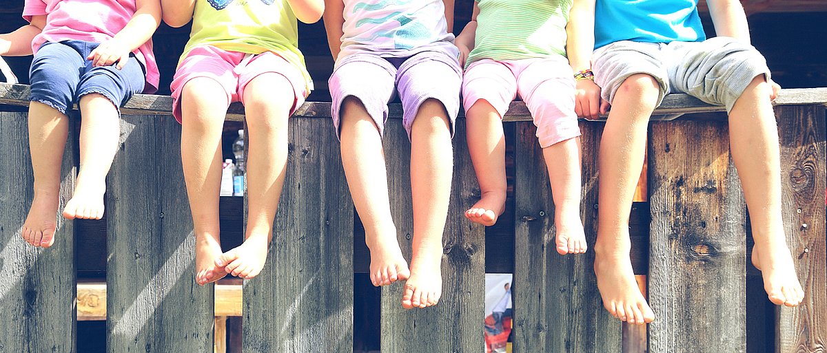 Kinder sitzen im Sommer mit nackten Füßen auf einem Holzgerüst