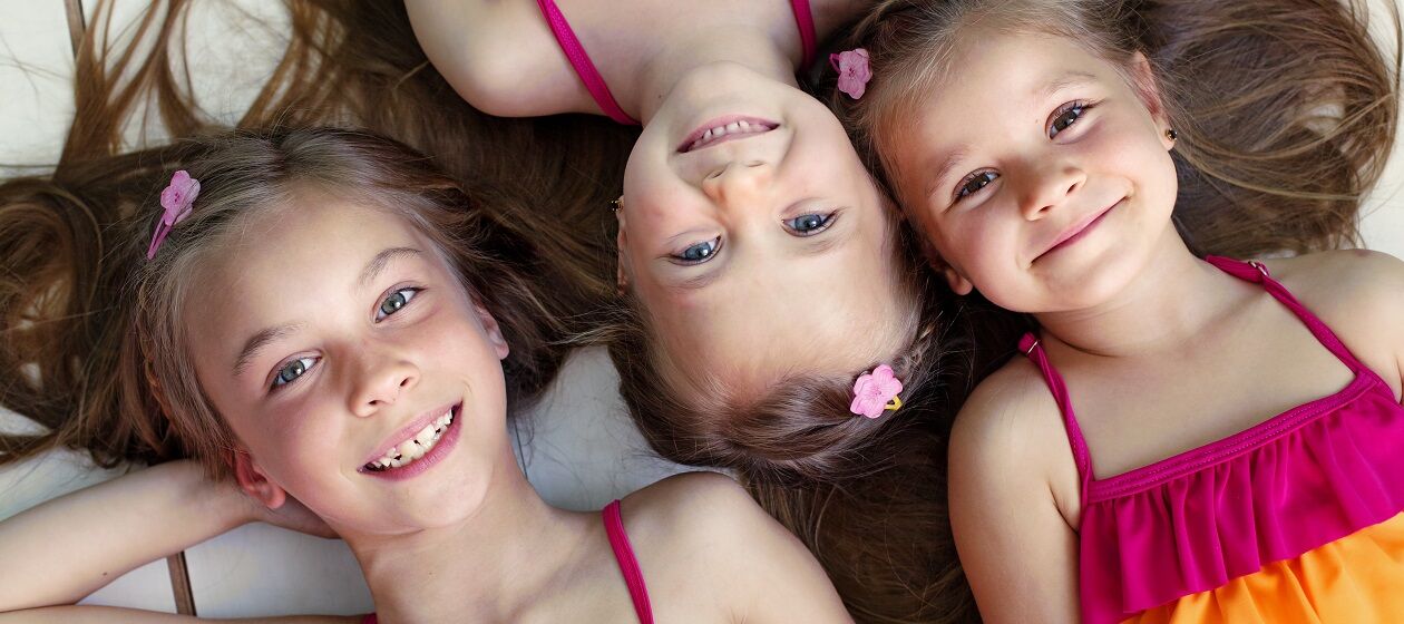 Drei Mädchen in unterschiedlichem Alter tragen das gleiche Kleid und lachen in die Kamera.