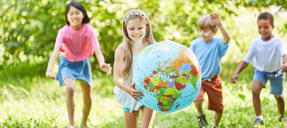 Ein Gruppe von Kindern unterschiedlicher Herkunft spielen in einem Park mit einem Globus-Wasserball.