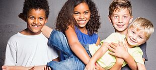 Vier Kinder unterschiedlicher Hautfarbe stehen lächeln als Gruppe zusammen