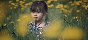 Ein Kind sitzt in einem Feld mit gelben Blumen
