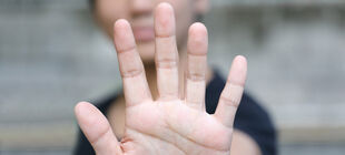 Eine junge Frau hält ihre ausgestreckte Hand zur Stopgeste vor ihr Gesicht. 