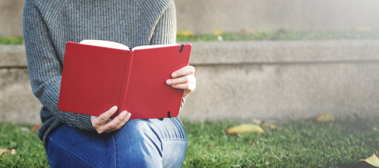 Eine Jugendliche sitzt draußen und liest in einem Buch
