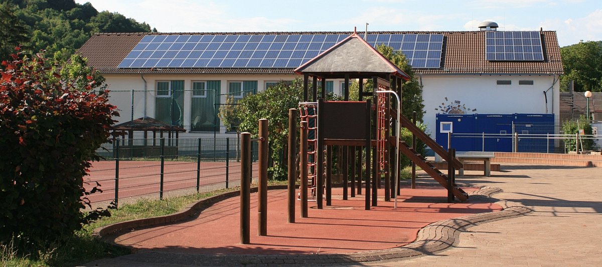 Ein Schulgebäude oder eine Kindertagesbetreuungsstätte, in dessen Vordergrund ein Spielplatz zu sehen ist