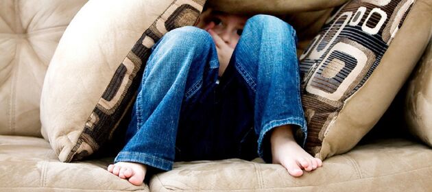 Ein Kind versteckt sich unter vielen Kissen auf dem Sofa.