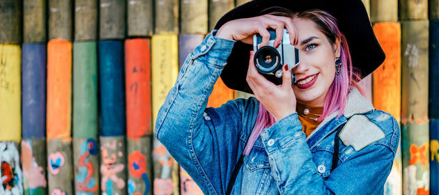 Eine junge Frau hält lächelnd einen klassischen Fotoapparat und stellt die Linse ein.