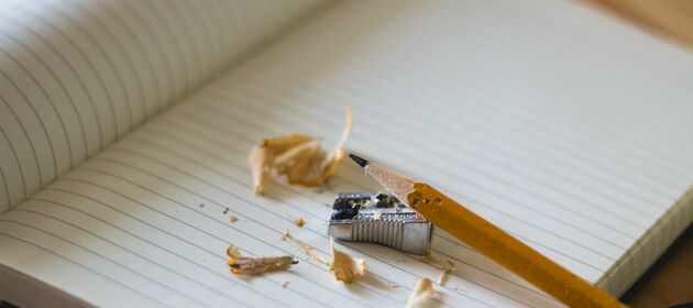Ein Bleistift liegt neben einem Anspitzer auf einem aufgeschlagenen, leeren Notizbuch