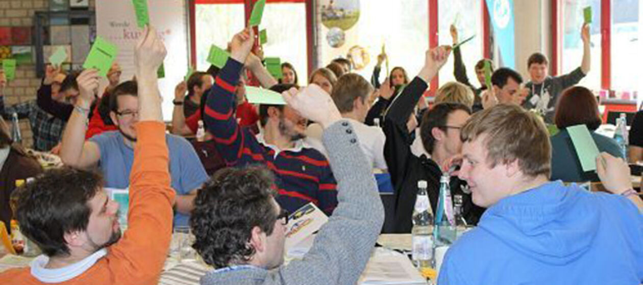 Junge Menschen halten bei einer Abstimmung Zettel in die Luft