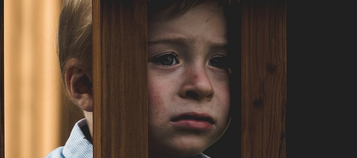 Ein Kind schaut traurig durch zwei Holzstreben