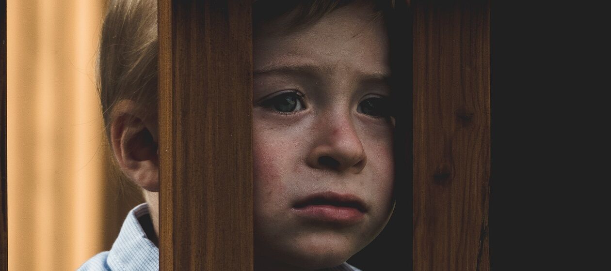 Ein Kind schaut traurig durch zwei Holzstreben