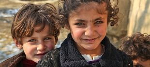 Ein Junge und ein Mädchen in Afghanistan blicken in die Kamera.
