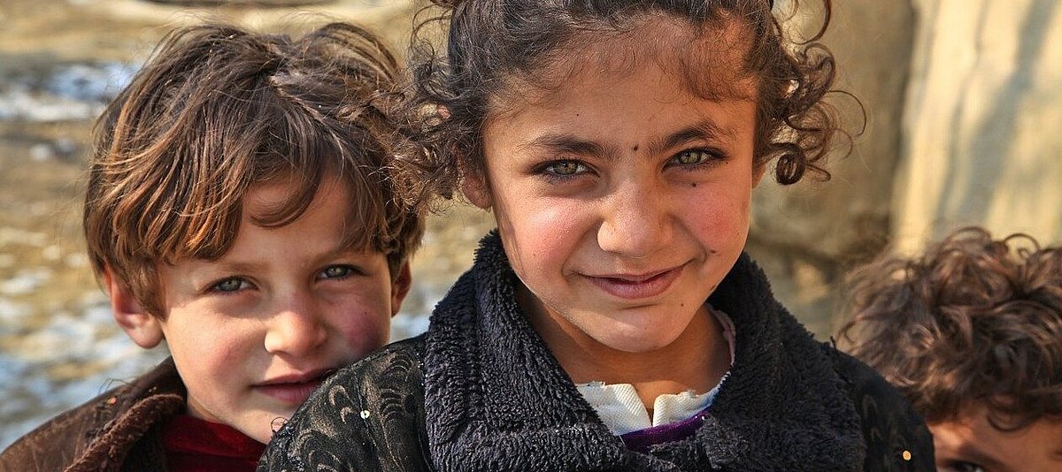 Ein Junge und ein Mädchen in Afghanistan blicken in die Kamera.
