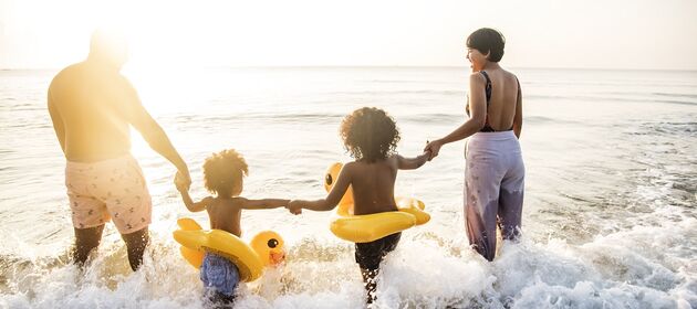 Zwei Erwachsene und zwei Kinder mit Schwimmreifen gehen ins Meer