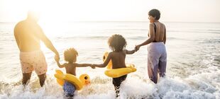 Zwei Erwachsene und zwei Kinder mit Schwimmreifen gehen ins Meer
