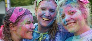 Drei Jugendliche mit von Farbpulver bunt befleckten Köpfen lachen.