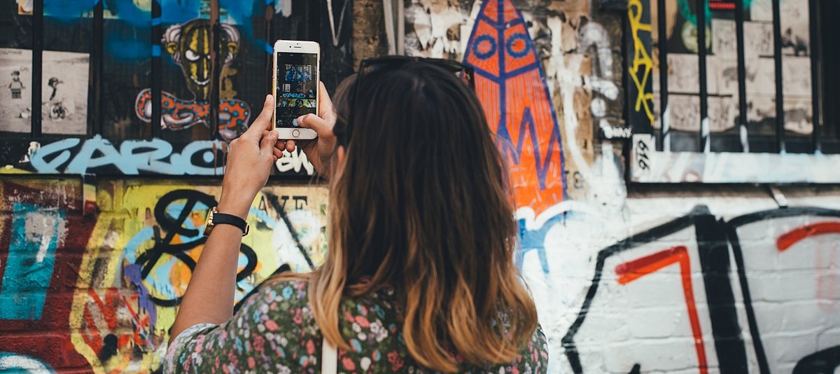 Eine Jugendliche macht mit ihrem Smartphone ein Fot von einer Graffitti-Wand