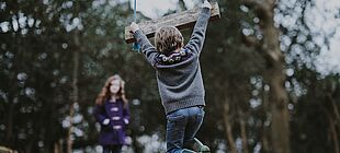 Ein Kind hängt sich eine Schaukel, im Hintergrund ist ein Wald zu sehen