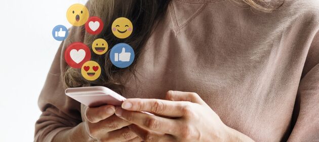 Hände halten ein Smartphone über dem Emojis aufploppen