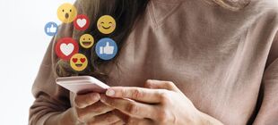 Hände halten ein Smartphone über dem Emojis aufploppen