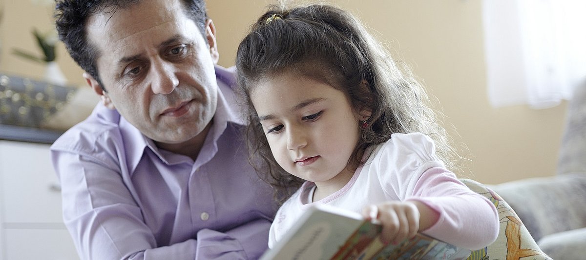 Ein Vater schaut seiner Tocher zu, wie sie in einem Buch blättert