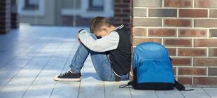Eine Junge sitzt einsam auf einem Schulflur und legt traurig seinen Kopf auf die Knie.