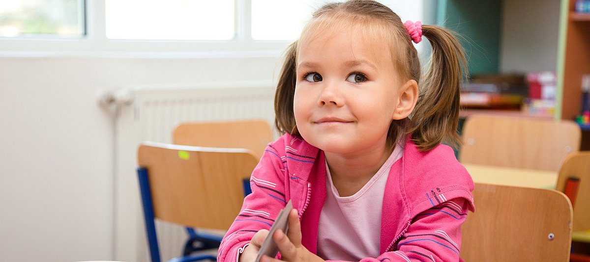 Ein Mädchen sitzt am Tisch in der Kindertageseinrichtung