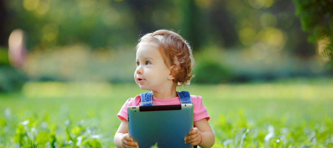 Kleinkind sitz mit Tablet auf einer Wiese