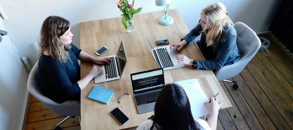 Drei Frauen sitzen mit ihren Laptopn gemeinsam an einem Tisch und arbeiten