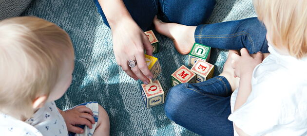 Eine Erwachsene spielt mit kleinen Kindern auf dem Teppich mit Bauklötzen