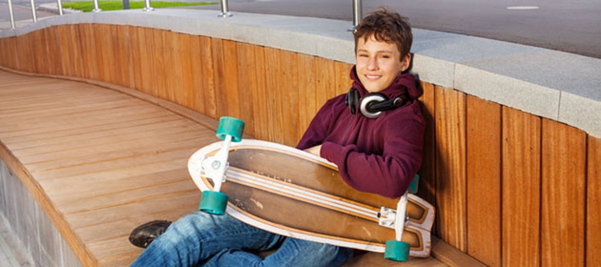 Ein Junge mit einem Skateboard fläzt sich auf einer Bank