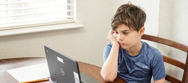 Ein Junge schaut unmotiviert auf einen Laptop