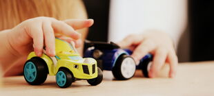 Nahaufnahme eines kleinen Kindes, das mit zwei Spielzeugautos spielt